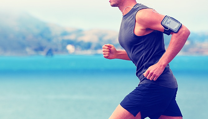 Cardio runner running listening smartphone music. Unrecognizable body jogging on ocean beach or wate