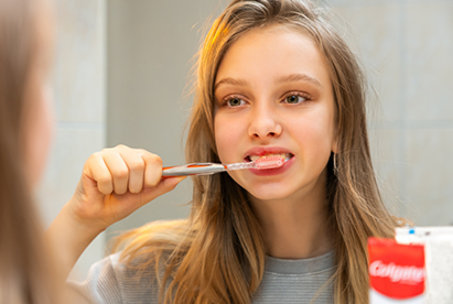 Woman smiling while adding Colgate toothpaste to a toothbrush in a bathroom.