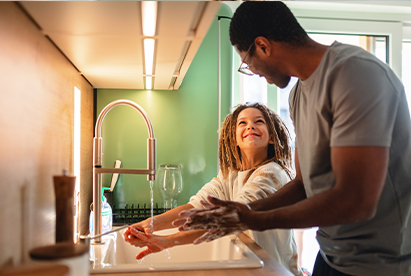 Father helping his daughter wash her hands with liquid soap at the kitchen sink, showcasing gentle skin care and hygiene for families.