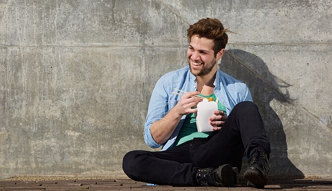 Cheerful young man eating chinese take away food with chopsticks 