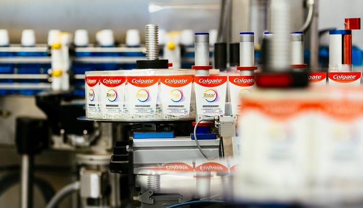 Multiple tubes of Colgate toothpaste using recyclable packaging on a machine.