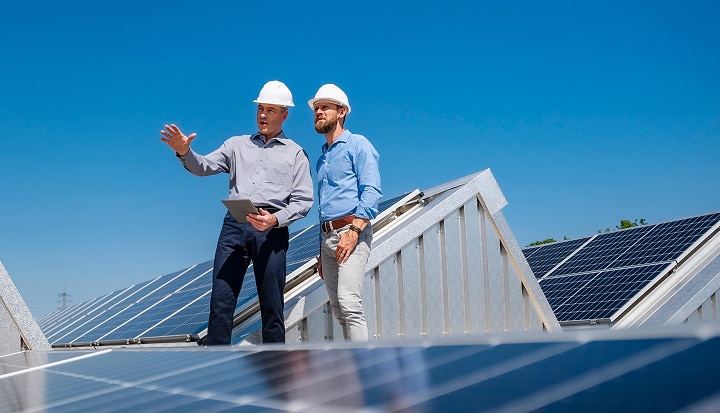 Two men talking while wearing hard hats in the middle of a solar farm.
