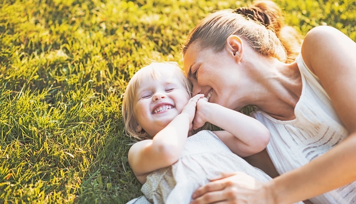 Mother and young child lying on the grass, laughing and enjoying a playful moment together in the sunshine