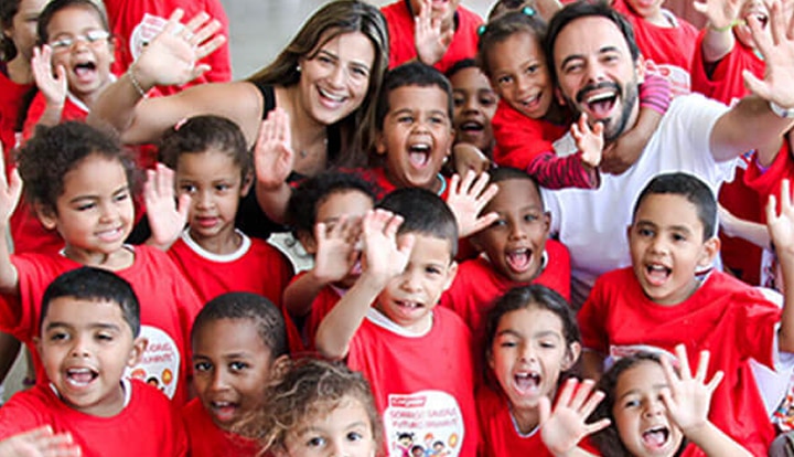 Group of children and adults smiling and waving at the camera while wearing "Bright Smiles, Bright Futures" shirts.