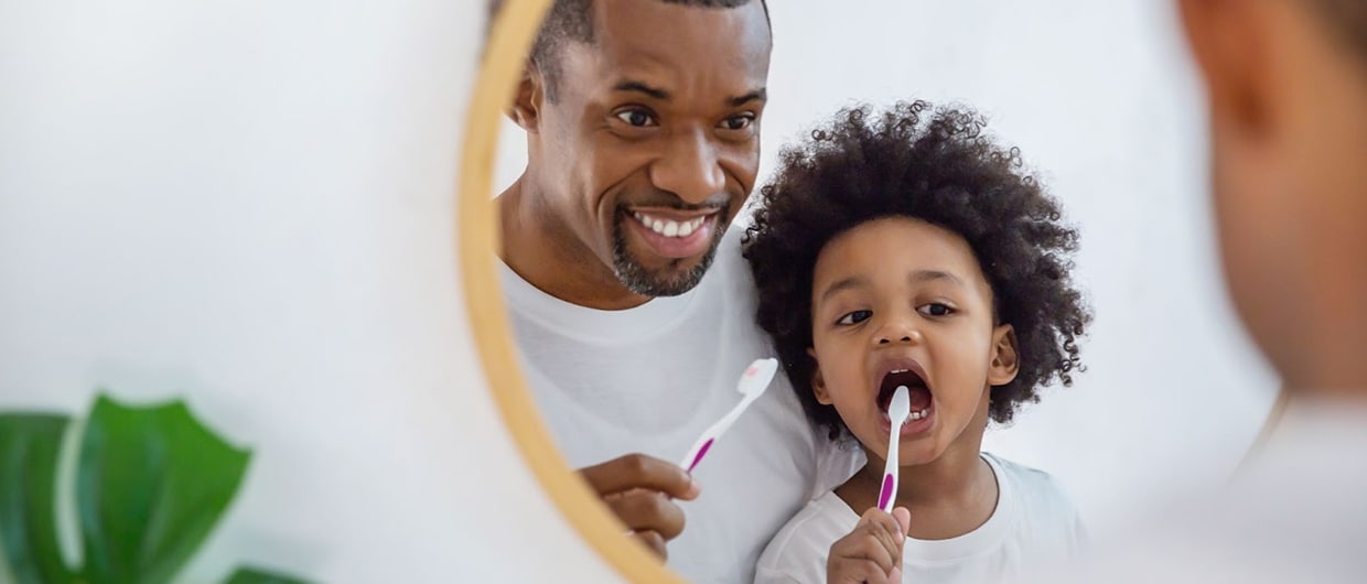 man and child brushing their teeth in front of a mirror