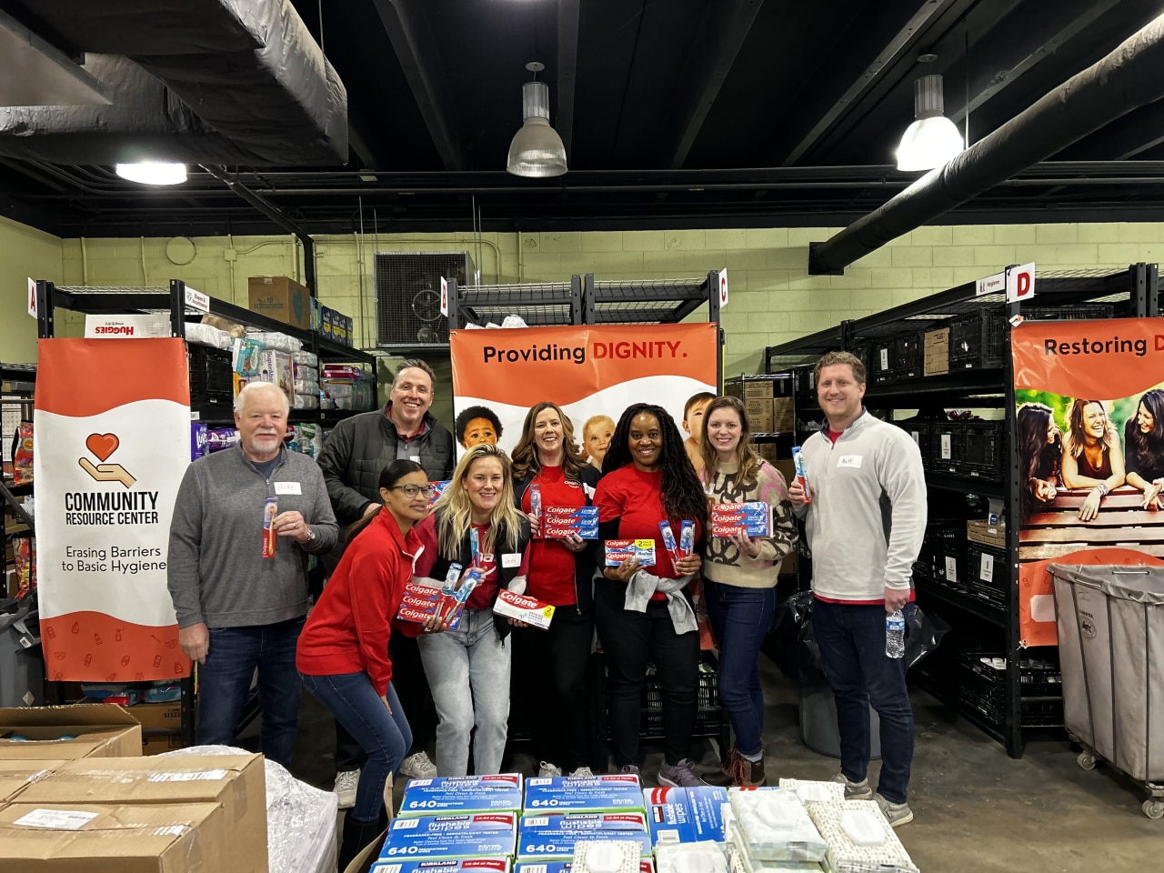 Group of Colgate employee volunteers posing with hygiene product donations at a Community Resource Center warehouse event.