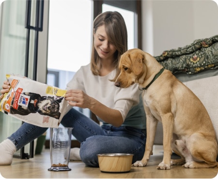 Naine valab Hill's Pet Nutritioni toitu mõõteanumasse, samal ajal kui koer seda tähelepanelikult jälgib.