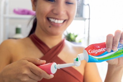 Naine naeratab, kui ta vannitoas paneb Colgate’i hambapastat hambaharjale.